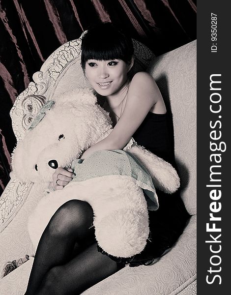 A beautiful Asian girl with teddy bear is watching television.