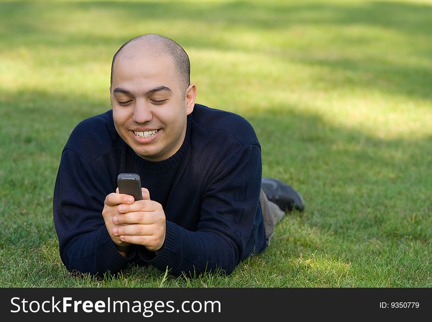 Young man lying on grass and messaging on the mobile phone. Young man lying on grass and messaging on the mobile phone