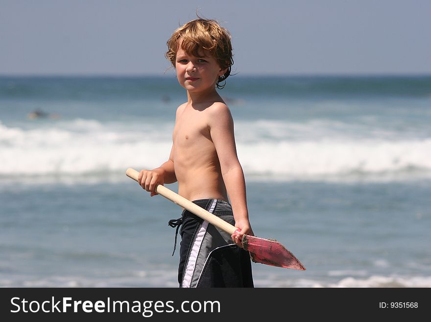 Young Boy hodin a red shovel at the beach. Young Boy hodin a red shovel at the beach