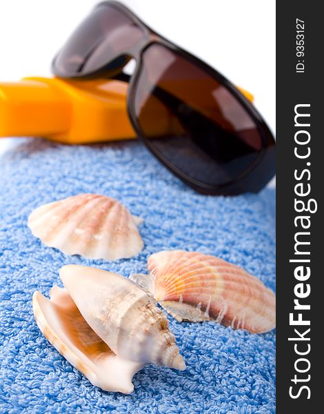 Towel, shells, sunglasses and lotion closeup on white background