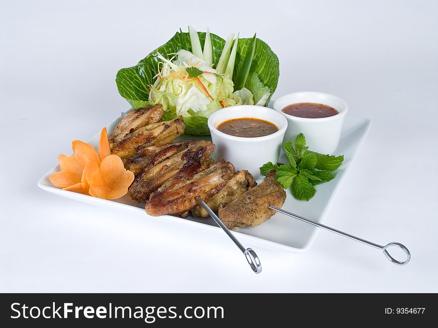 Chicken wing skewers with a salad and dipping sauce isolated on a white background
