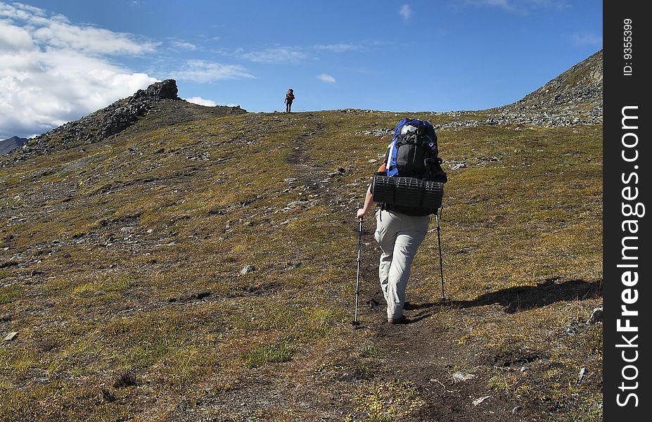 Two female backpackers walk along an alpine hillside trail in Tombstone Territorial Park, Yukon Territory. Two female backpackers walk along an alpine hillside trail in Tombstone Territorial Park, Yukon Territory