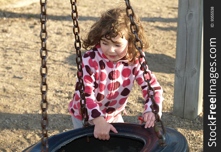 Young preschooler having fun at a playground with a tire swing suspended from chains. Young preschooler having fun at a playground with a tire swing suspended from chains.