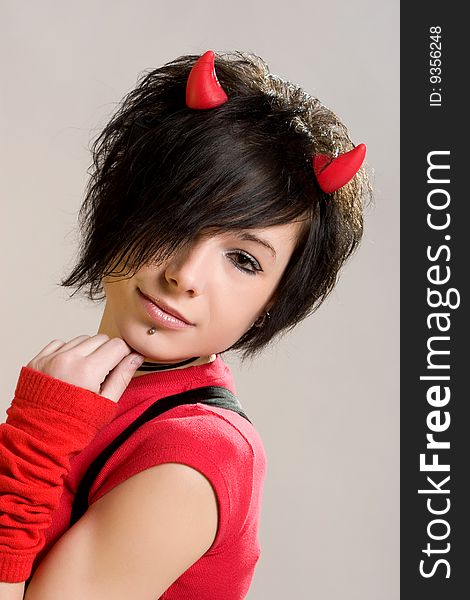 A young sexual girl in an image of a  devil  in red and black with   horns on her head posing on a light background. A young sexual girl in an image of a  devil  in red and black with   horns on her head posing on a light background