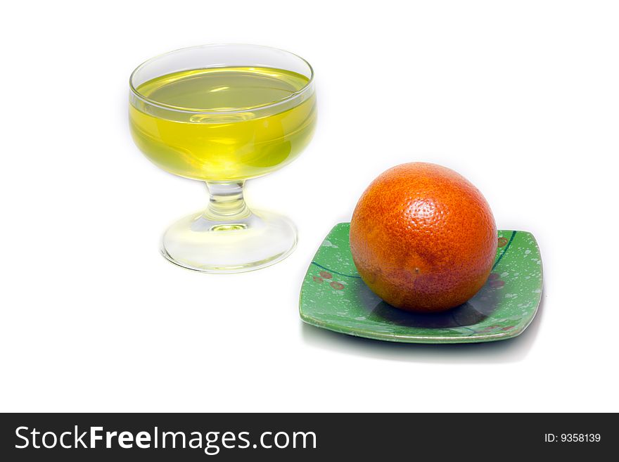 Yellow jelly but transparent glass and orange on green saucer on white background