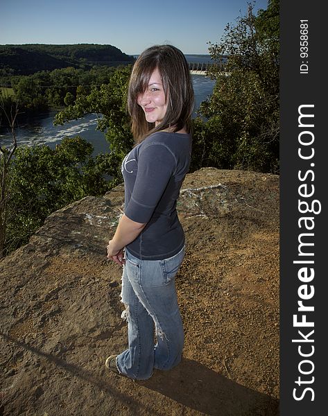 A teen girl strikes a playful pose on a ledge overlooking a river. A teen girl strikes a playful pose on a ledge overlooking a river.