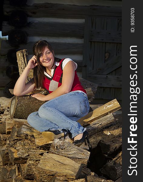 Teenager sits on pile of logs outside cabin. Teenager sits on pile of logs outside cabin.