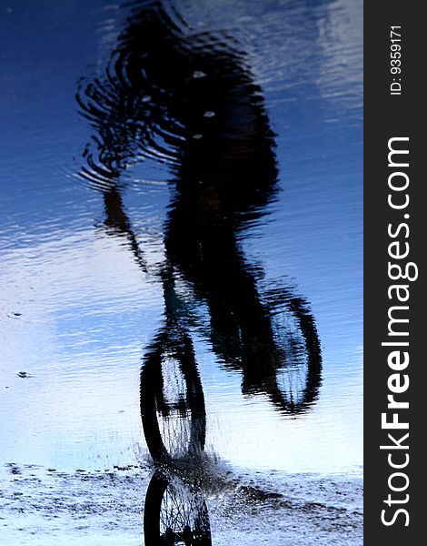 Athlete cycling is reflected in the water against the background of blue sky. Athlete cycling is reflected in the water against the background of blue sky