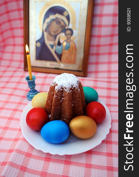 Easter still-life. Orthodox religion. An icon, a candle, an Easter cake, multi-coloured eggs.