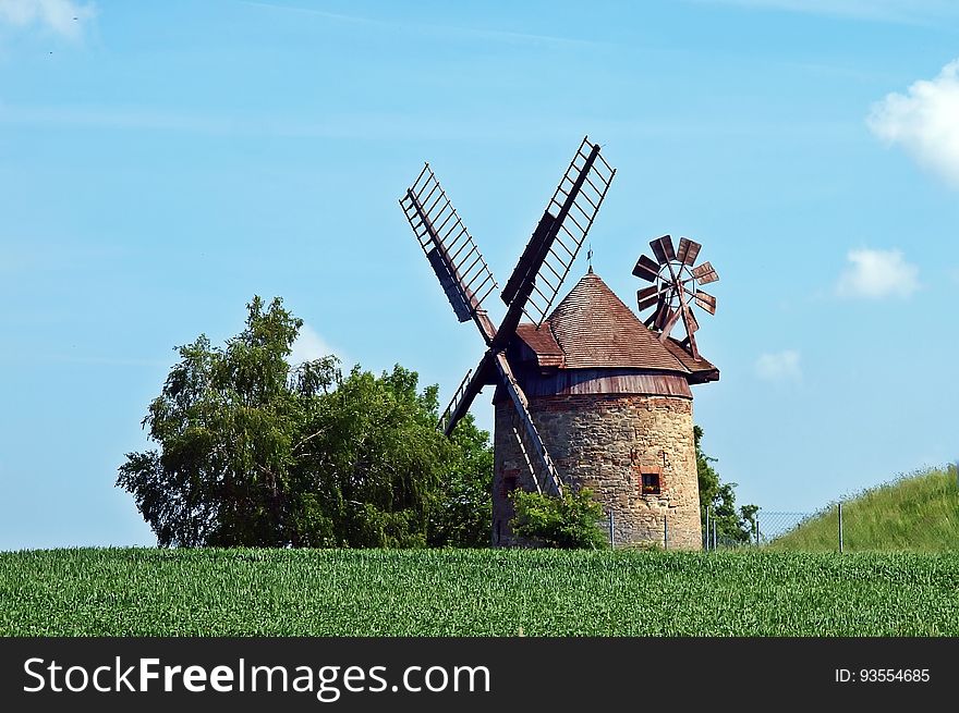 Brown and Gray Windmill Beside Green Tree Under Blue Cloudy Sky during Day Time