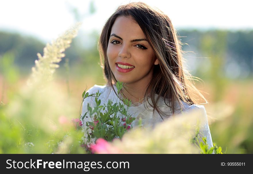 Woman in White Crew Neck Shirt Smiling and Surround With Flowers and Plants during Daytime