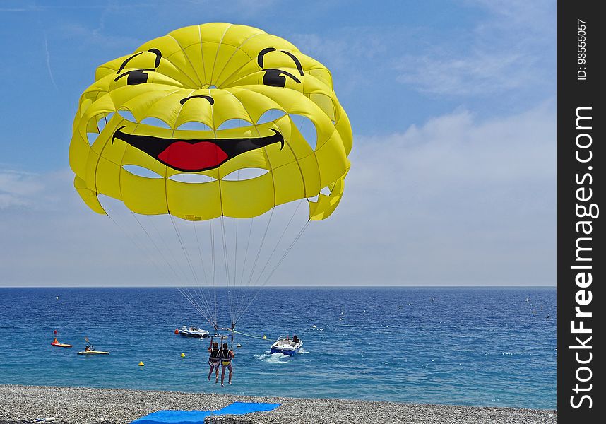 People parasailing over a beach with a yellow smiley parachute. People parasailing over a beach with a yellow smiley parachute.