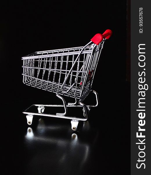 A close up of a chrome shopping cart with a red handle.