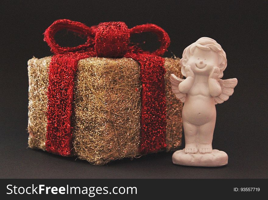 A Christmas present with a red ribbon and a miniature angel statue. A Christmas present with a red ribbon and a miniature angel statue.