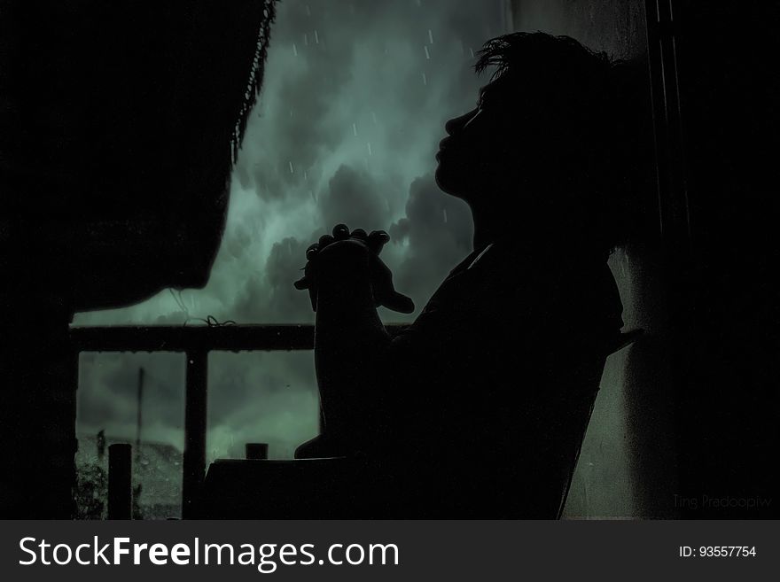A silhouette of a pensive man sitting on a balcony in the rain at night. A silhouette of a pensive man sitting on a balcony in the rain at night.