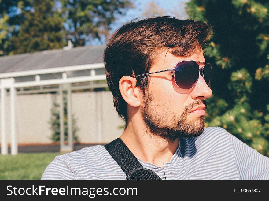 A man with sunglasses and beard sitting outdoors in the sunshine.