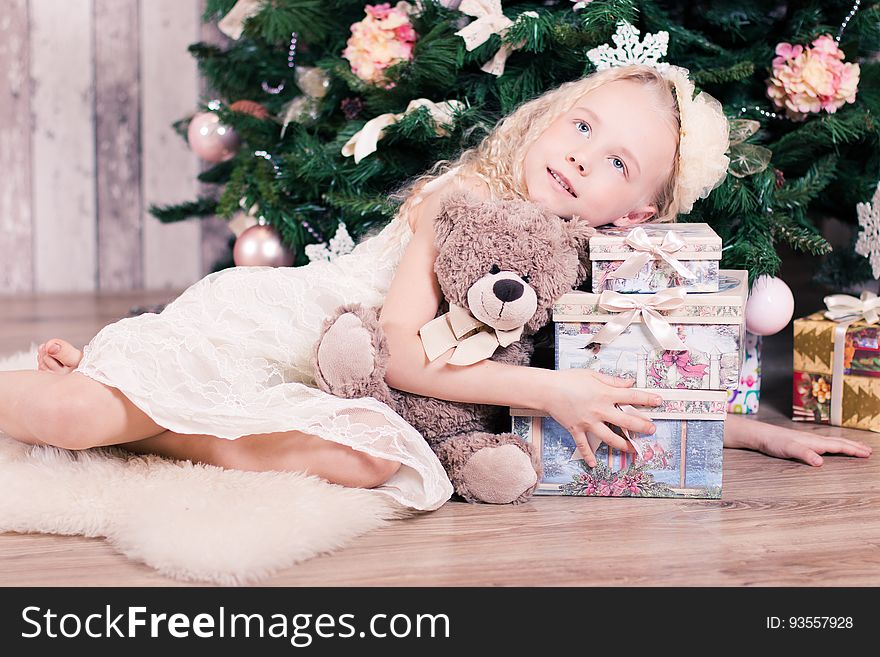 A girl holding a teddy bear and a pile of Christmas presents under a Christmas tree. A girl holding a teddy bear and a pile of Christmas presents under a Christmas tree.