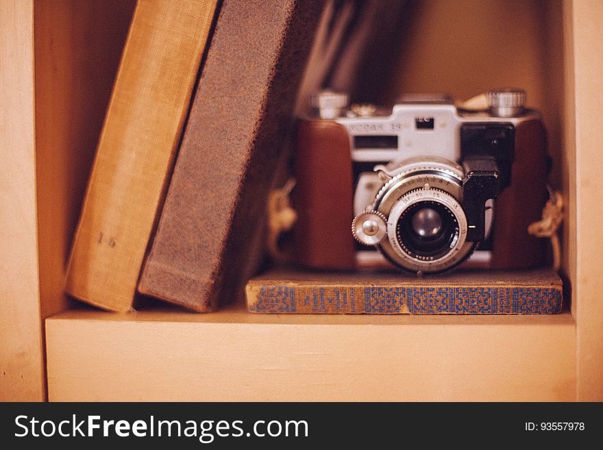 An old analog film camera in a bookshelf with books. An old analog film camera in a bookshelf with books.