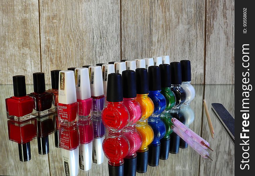 Colorful nail polish bottles with brush and file reflecting on glass background.