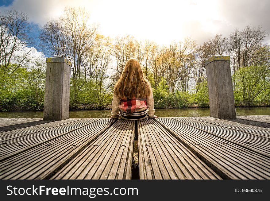 A girl sitting on a pier at lake or pond. A girl sitting on a pier at lake or pond.