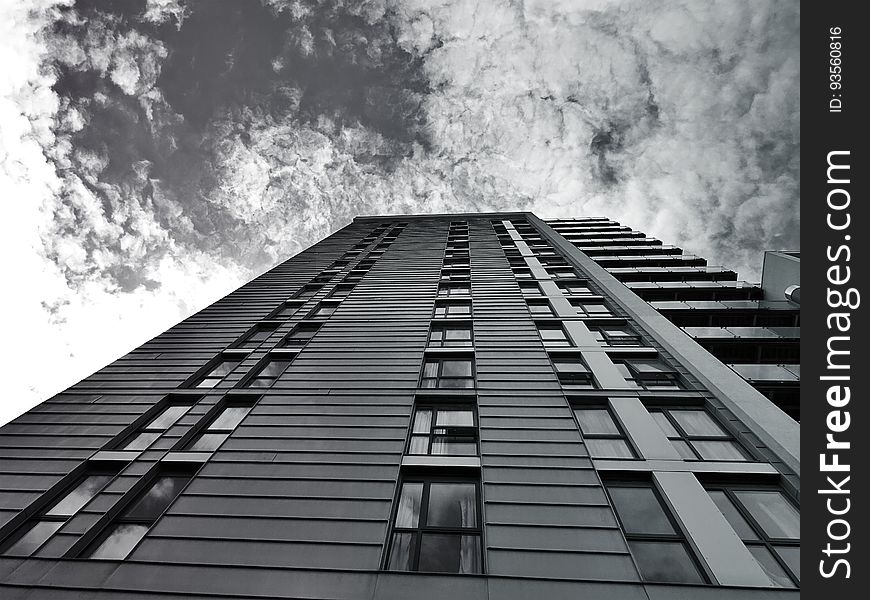 Low angle black and white view looking to top of modern high rise building with cloudscape background. Low angle black and white view looking to top of modern high rise building with cloudscape background.
