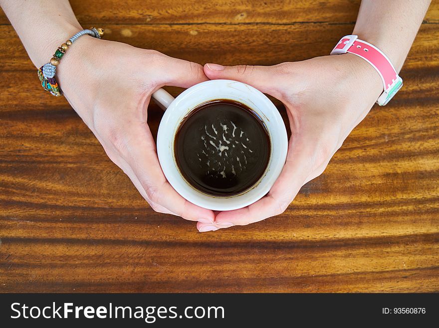 A woman holding a cup of coffee with both hands. surface. A woman holding a cup of coffee with both hands. surface