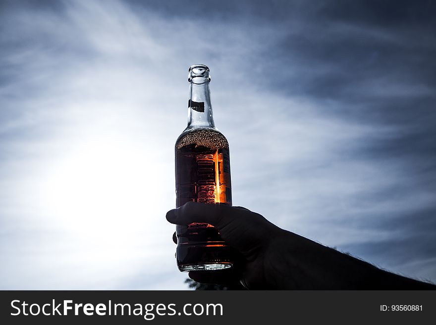 A person holding up a bottle of beverage against the sky. A person holding up a bottle of beverage against the sky.
