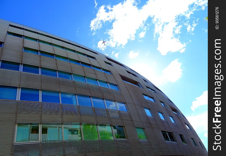 Glass and concrete building (apartments or offices) architecturally designed with a curved facade and with reflections of the blue sky and on lower floor of green trees. Glass and concrete building (apartments or offices) architecturally designed with a curved facade and with reflections of the blue sky and on lower floor of green trees.