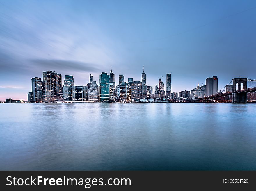 Skyscrapers of Manhattan, New York skyline against blue skies at sunrise over riverfront with Brooklyn Bridge. Skyscrapers of Manhattan, New York skyline against blue skies at sunrise over riverfront with Brooklyn Bridge.