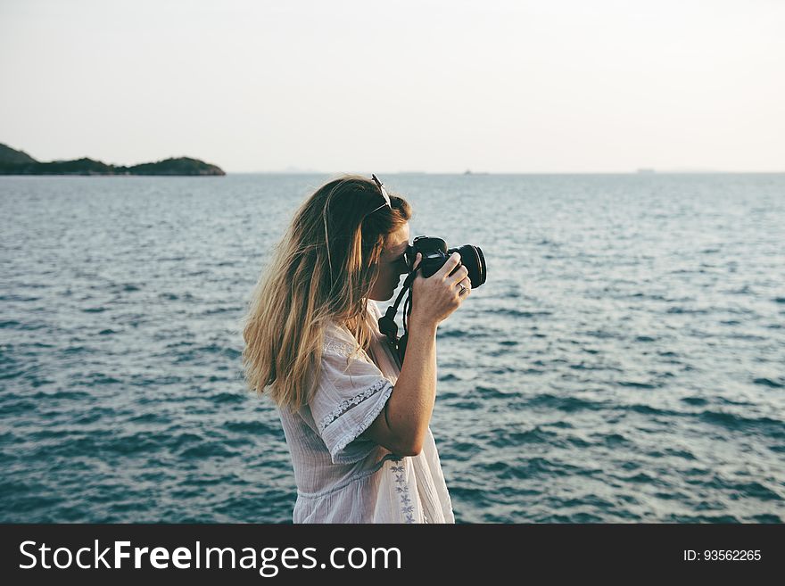 A woman standing on a beach with a camera taking photos. A woman standing on a beach with a camera taking photos.