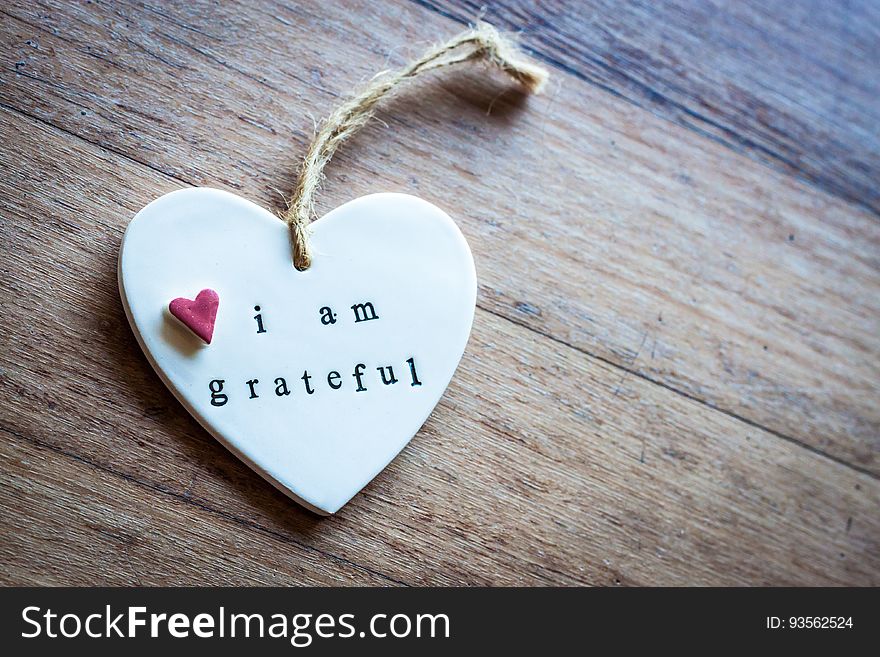 Close up of white china heart ornament with message i am grateful on rustic wooden boards.