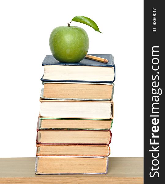 Green ripe apple and pencil on pile of books