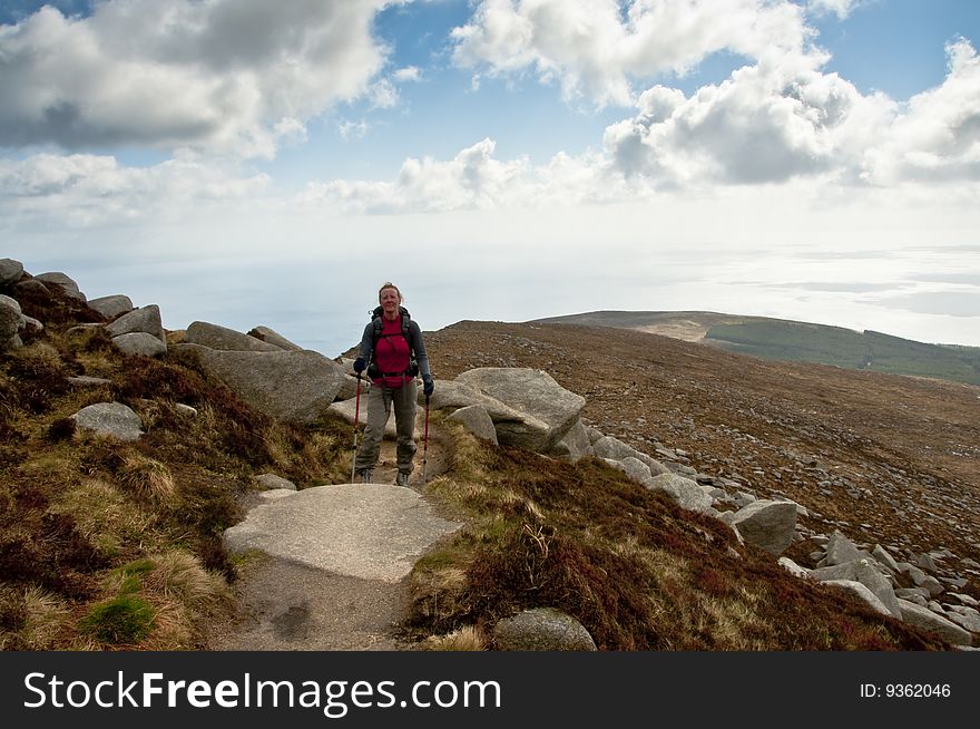 Woman walker with trekking poles on path in the mountains. Woman walker with trekking poles on path in the mountains