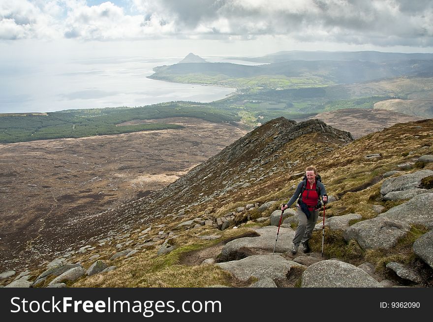 Woman walker with trekking poles on path in the mountains. Woman walker with trekking poles on path in the mountains