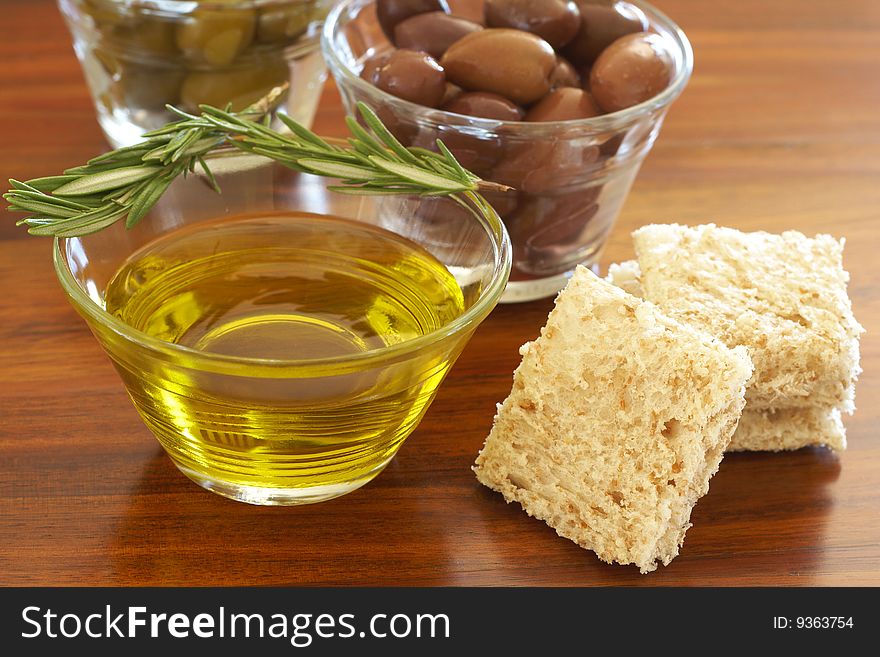 Two jars of green and black olives with stick of rosemary, olive oil and slices of bread on wooden table background. Two jars of green and black olives with stick of rosemary, olive oil and slices of bread on wooden table background