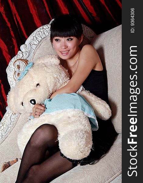 A Asian girl is holding the teddy bear and watching TV . A Asian girl is holding the teddy bear and watching TV .