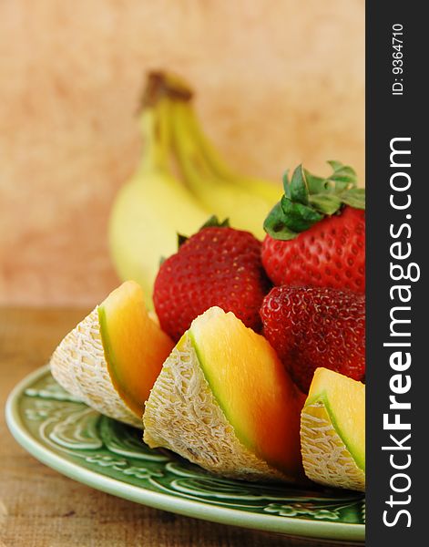 Sliced Cantaloupe and strawberries on a wooden table with a pink background.