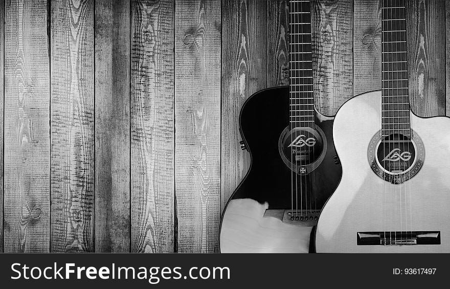 Vintage wooden acoustic guitars leaning against rustic wood planks in black and white. Vintage wooden acoustic guitars leaning against rustic wood planks in black and white.