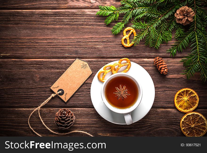 Christmas still life with green pine boughs, pine cones, orange slices and cup of tea in white cup and saucer on rustic wooden boards with blank gift tag. Christmas still life with green pine boughs, pine cones, orange slices and cup of tea in white cup and saucer on rustic wooden boards with blank gift tag.