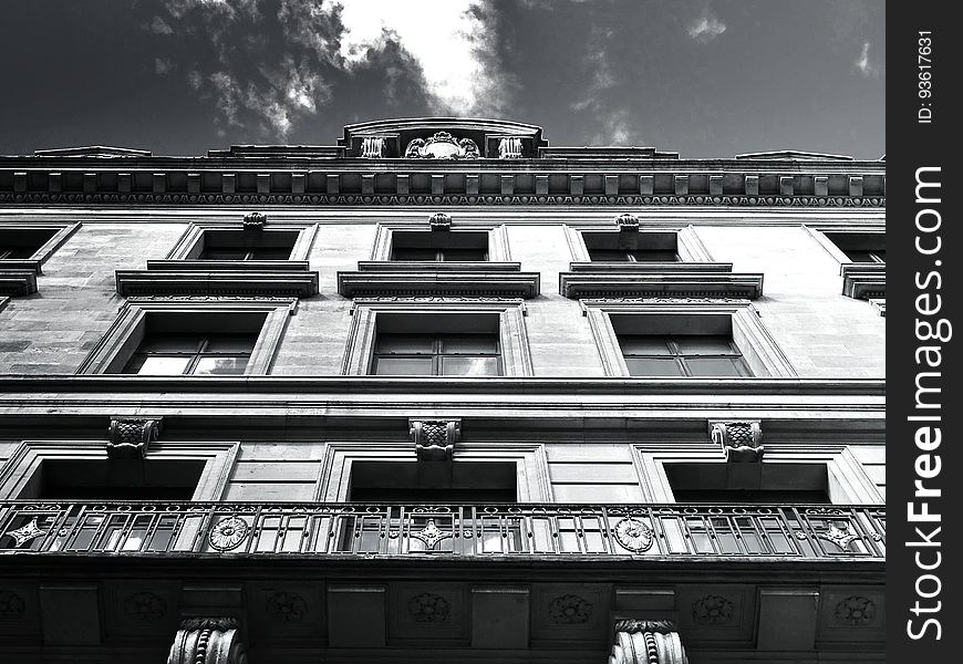 Front of apartment building with balconies and window against cloudy skies in black and white.