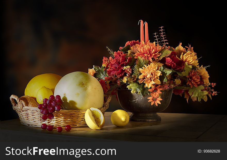 An autumn flower arrangement sitting next to a fruit basket. An autumn flower arrangement sitting next to a fruit basket.