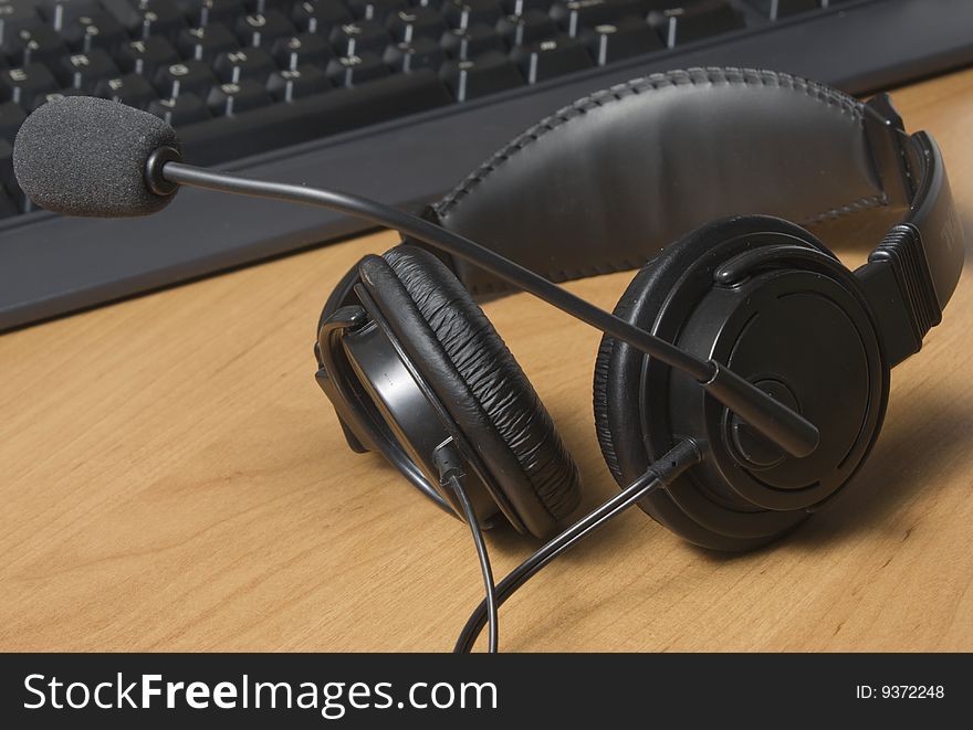 A headset and keyboard sit on a wood desk