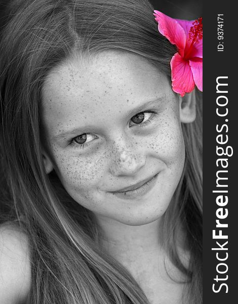 A white caucasian kid smiling with a flower in her hair. Picture in black and white with flower in pink. A white caucasian kid smiling with a flower in her hair. Picture in black and white with flower in pink