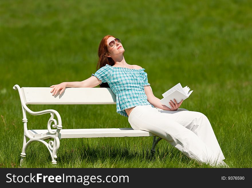 Summer - Young woman on white bench with book enjoying sun in green meadow