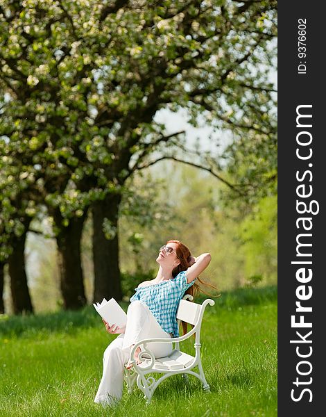 Summer - Red hair woman sitting on white bench in green meadow, shallow DOF. Summer - Red hair woman sitting on white bench in green meadow, shallow DOF
