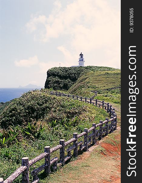 A trail leads to a lighthouse on a hill by the sea. A trail leads to a lighthouse on a hill by the sea