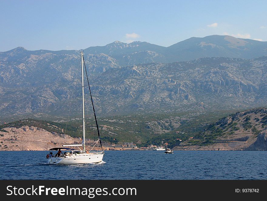 The yacht on calm sea with mountain in background.