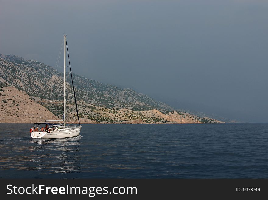 The yacht on calm sea with dark sky on background.