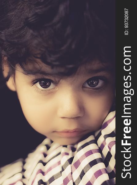 Portrait of young boy with brown curly hair and brown eyes leaning on striped pillow.