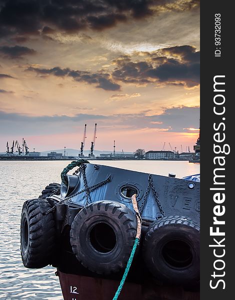 Tires tied to ship on shoreline of harbor with dock at sunset. Tires tied to ship on shoreline of harbor with dock at sunset.